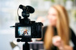 © artiemedvedev - Display of camera recording video blog for blonde beauty blogger woman with make-up at home studio. Influencer vlogger girl live streaming cosmetics masterclass. Online learning and marketing concept.