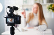 © artiemedvedev - Display of camera recording video blog for blonde beauty blogger woman with make-up at home studio. Influencer vlogger girl live streaming cosmetics masterclass. Online learning and marketing concept.