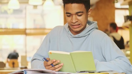 Poster - Handsome concentrated young african  guy student studying doing homework reading book.