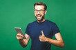 © denis_vermenko - Winner! Happy young man in casual shirt and glasses standing and using tablet over green background. Thumbs up.