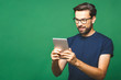 © denis_vermenko - Happy young man in casual shirt and glasses standing and using tablet over green background