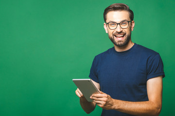 Wall Mural - Happy young man in casual shirt and glasses standing and using tablet over green background