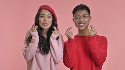 Poster - Young happy cute loving couple isolated over pink wall background make heart gesture.