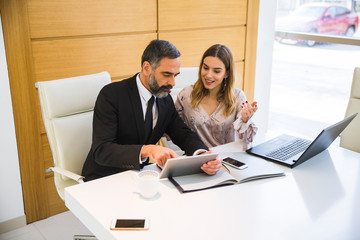 Handsome mature man with digital tablet and young woman business partners with laptop working in office