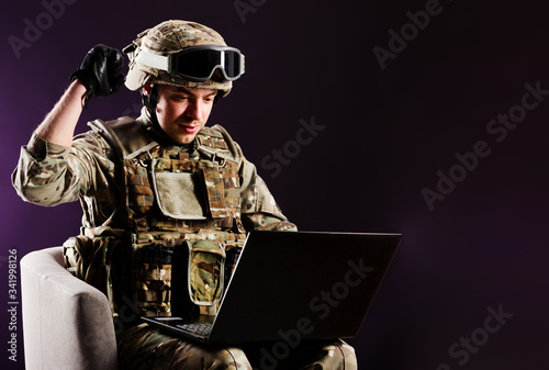 Fotomural Man gamer with laptop is celebraiting the win in soldier clothes on brown background
