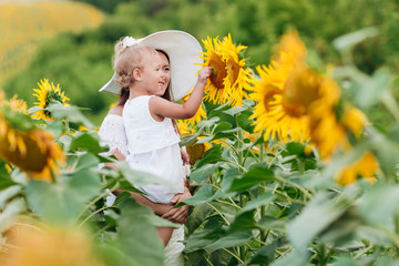 Wall Mural - Happy mother with the daughter in the field with sunflowers. mom and baby girl having fun outdoors. family concept. selective focus