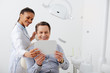 © LIGHTFIELD STUDIOS - happy patient looking at mirror near cheerful african american dentist in braces