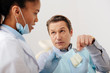 © LIGHTFIELD STUDIOS - selective focus of man pointing with finger at teeth model near african american dentist in latex gloves