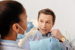 © LIGHTFIELD STUDIOS - selective focus of african american dentist in latex gloves holding dental floss near patient pointing with finger at face