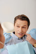 © LIGHTFIELD STUDIOS - selective focus of african american dentist in latex gloves holding dental floss near handsome patient pointing with finger at face