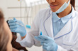 © LIGHTFIELD STUDIOS - cropped view of african american dentist in latex gloves holding toothbrush and inter dental cleaning brush near patient