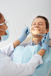 © LIGHTFIELD STUDIOS - selective focus of african american dentist in medical mask and face shield holding dental instruments near happy patient