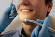 © LIGHTFIELD STUDIOS - cropped view of dentist in latex gloves holding dental instruments near cheerful patient