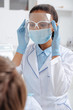 © LIGHTFIELD STUDIOS - selective focus of african american dentist in medical mask touching face shield near patient