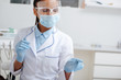 © LIGHTFIELD STUDIOS - african american dentist in medical mask, face shield and latex gloves pointing with finger in clinic