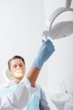 © LIGHTFIELD STUDIOS - selective focus of african american dentist in latex glove touching medical lamp near patient