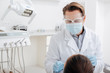 © LIGHTFIELD STUDIOS - selective focus of dentist in face shield, medical mask and latex gloves near woman