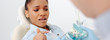© LIGHTFIELD STUDIOS - panoramic shot of scared african american woman in braces pointing with finger at teeth model near dentist