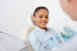 © LIGHTFIELD STUDIOS - selective focus of happy african american woman in braces near dentist holding teeth model