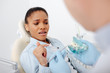 © LIGHTFIELD STUDIOS - selective focus of scared african american woman in braces pointing with finger at teeth model near dentist