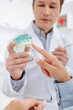 © LIGHTFIELD STUDIOS - selective focus of dentist in white coat near patient pointing with finger at teeth model