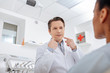 © LIGHTFIELD STUDIOS - selective focus of dentist pointing with fingers at face and looking at african american patient