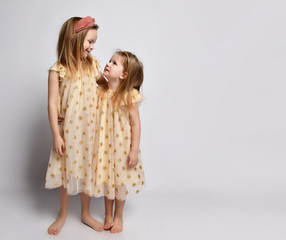 Two small beautiful smiling girls sisters in same dresses with stars barefoot standing, hugging and looking at each other