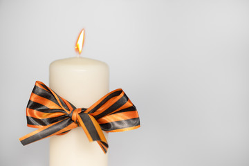 St. George's ribbon tied with a bow on a burning white candle on a white background: space for text