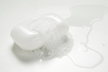 A wet bar of regular white soap bar with bubbles and water.