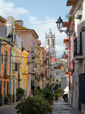 Fototapeta Uliczki - A busy and colourful Old Town street with bushes in the foreground and a traditional church visible through the buildings