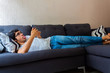 © Antonio Tanaka - Young Hispanic man with glasses, resting on a sofa, using his cell phone for various things