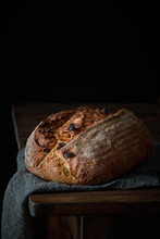 Crispy Freshly Baked Sourdough Bread Loaf With Raisin Placed On Gray Cloth On Wooden Table With Black Background