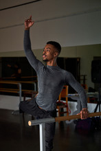 Professional Ballet Dancer Looking Away With Leg Up While Training In A Modern Studio Using Wooden Handrail