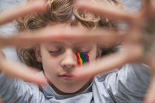 Top View Of Boy With Colorful Rainbow Under Eye With Eyes Closed Showing Stop Gesture With Hands With Stay Home Inscription To The Camera While Lying On Pillow And Blanket On Floor
