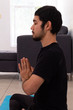 © Antonio Tanaka - young hispanic man wearing black sportswear meditating in a yoga session in the lotus flower pose , at home