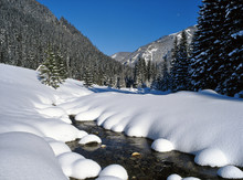 Stream Flowing Through Snow Covered Field Against Clear Blue Sky During Winter