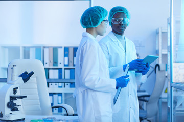 two scientists in white coats discussing scientific experiment together while working at the laborat