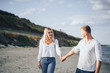 © Daria - Happy young couple having fun at beach on sunny evening. Smiling teens on vacation. Laughing couple in love holding hand enjoying summertime. Guy leading his girlfriend