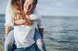 © Daria - Attractive blonde girl jumped onto her boyfriend's back. He carries her, she laughs and kisses him. They run along the sand on the seashore on a summer evening, lit by the sun. Romantic Date Concept