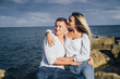 © Daria - Two lovers blondes spending a romantic evening on the beach. They  feeling evening sun, hugging, kissing and laughing, sitting on the worm stones. The girl is sitting on the arms of a guy.
