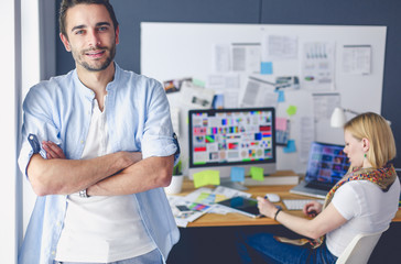 Poster - Portrait of young designer in front of laptop and computer while working. Assistant using her mobile at background.