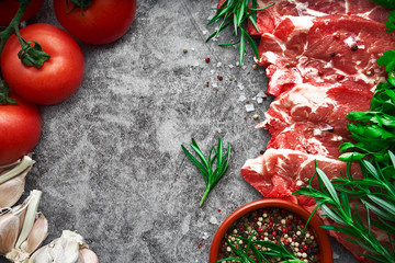 Raw beef steak with tomato, garlic, pepper, salt and rosemary on frying pan on a dark background. Food concept.