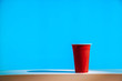 A disposable red plastic party beer cup on a white table or shelf with a bright modern blue background.