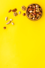 Wall Mural - Mixed nuts in bowl on yellow background top-down frame copy space