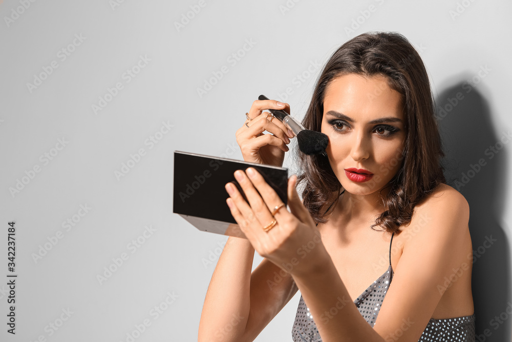 Beautiful young woman applying makeup against light background