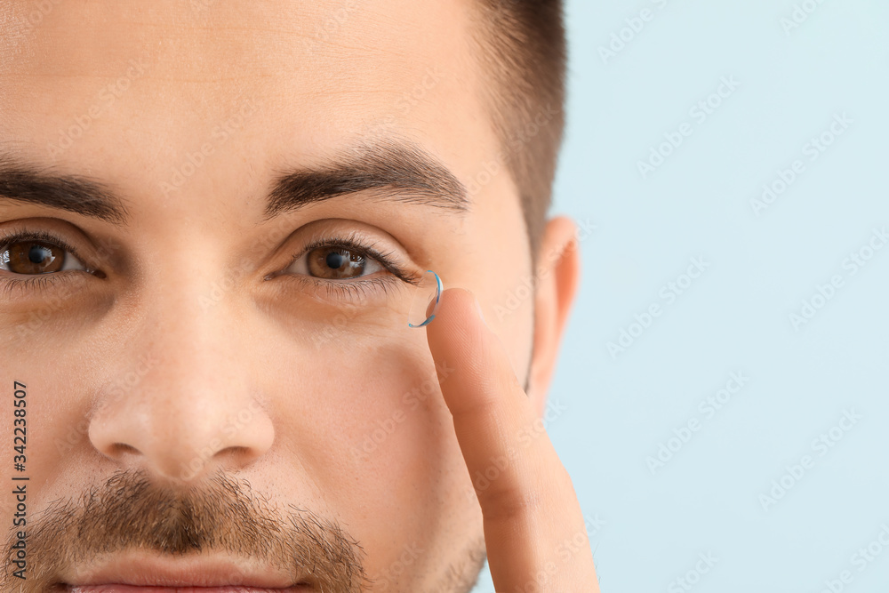 Young man with contact lens on color background, closeup