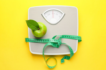 Weight scales with measuring tape and apple on color background. Slimming concept