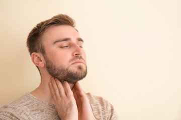 Young man checking thyroid gland on color background