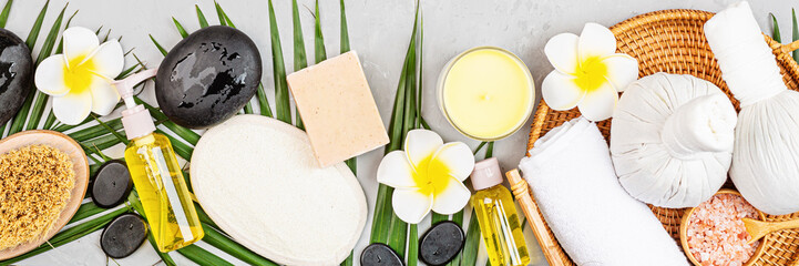 Poster - Spa massage Aromatherapy body care background. Spa herbal balls, cosmetics, towel and tropical leaves on gray concrete table. Top view, flat lay, overhead. Beauty and health care concept