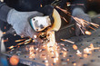 A metal worker cuts a rectangular metal pipe with an angle grinder